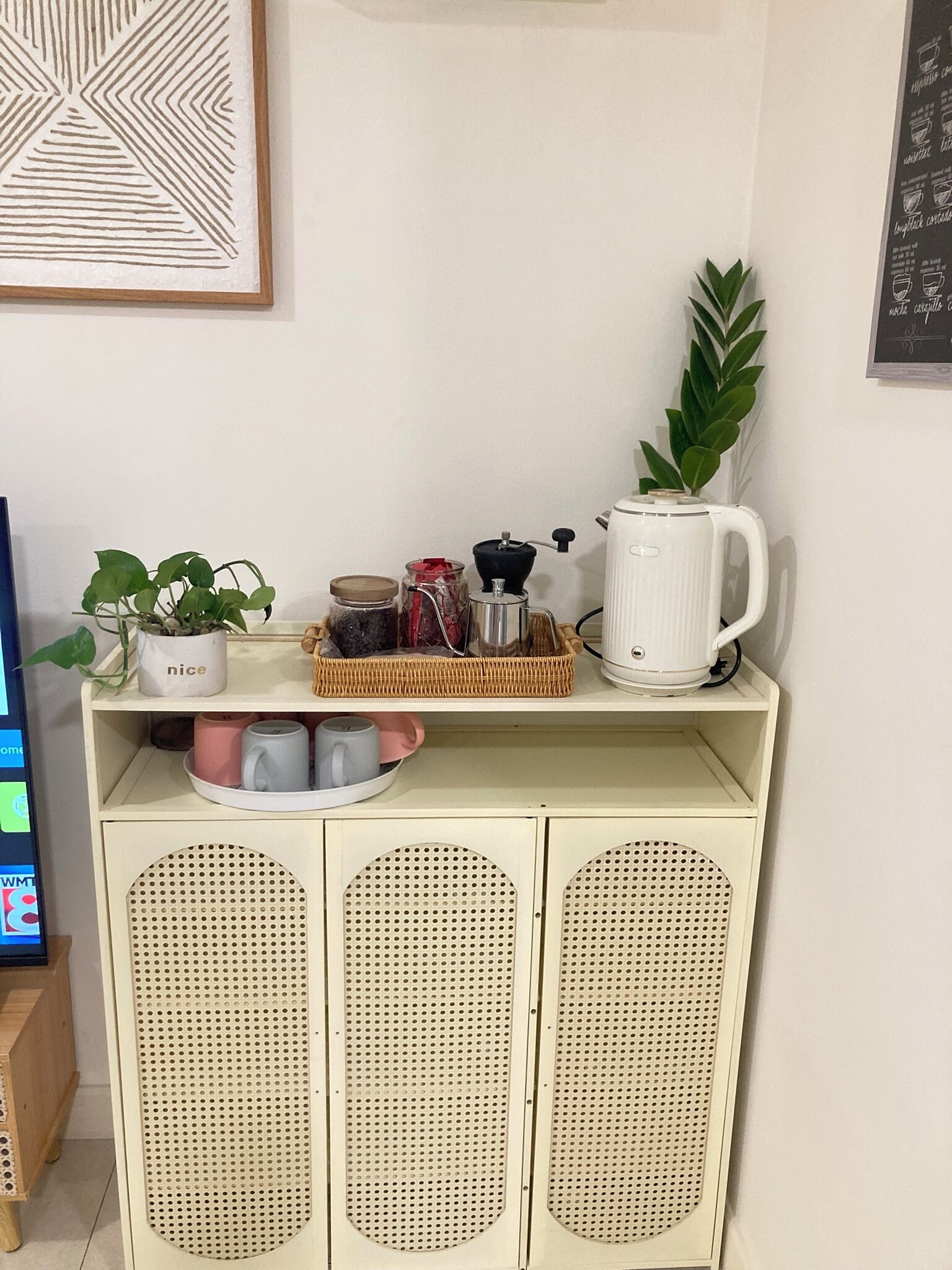 A kitchenette with a coffee maker, jars, a plant, and a shelf with mugs.