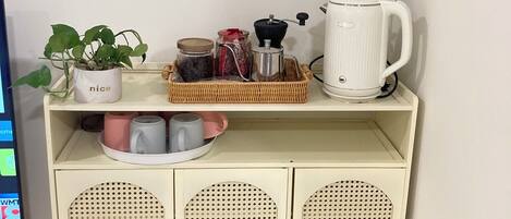 A kitchenette with a coffee maker, jars, a plant, and a shelf with mugs.