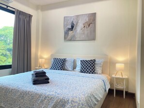 Una camera d'albergo con un letto, due lampade sui comodini, un quadro appeso e una finestra con tende.