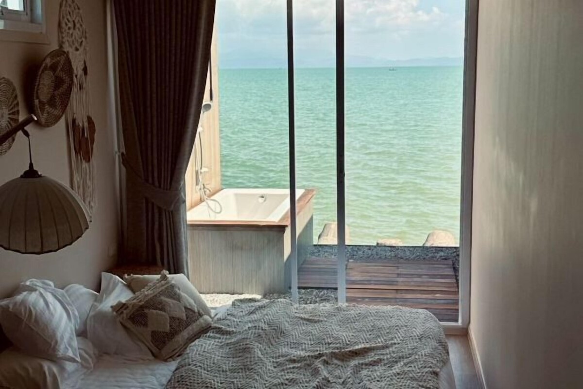 A bedroom with a bed, a window with a view of the sea, a bedside lamp, and a wall decoration.