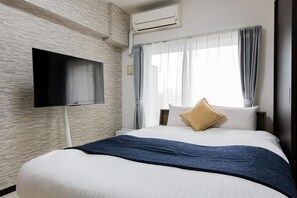 A hotel room with a bed, a flat-screen TV mounted on the wall, a window with curtains, and an air conditioning unit. - SPAZIO 2 Canal Hakata Annex (Fukuoka)