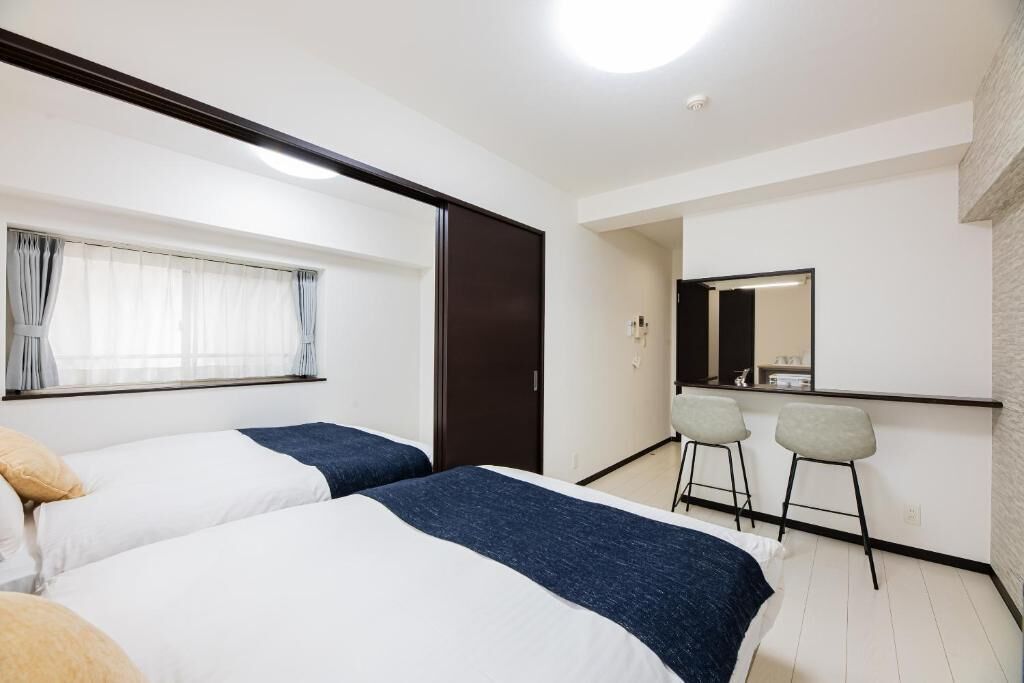 Habitació d'hotel amb dos llits, una cuineta petita i un mirall sobre el taulell.