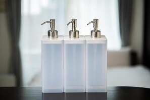 Trois flacons en verre transparent, équipés de pompes, portant les étiquettes « Après-shampoing » et « Savon pour le corps », placés sur une surface réfléchissante.