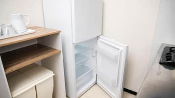 A compact kitchen with a white refrigerator, a wooden shelf, and a stainless steel sink.