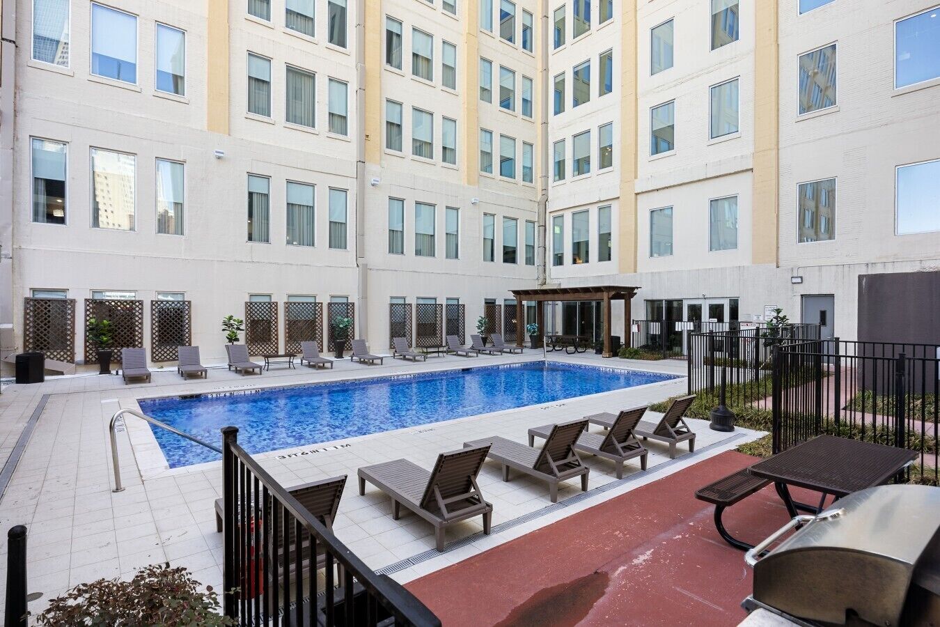 A hotel courtyard with a swimming pool, lounge chairs, and a barbecue area.
