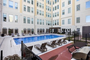 A hotel courtyard with a swimming pool, lounge chairs, and a barbecue area. - Modern City Stay | Pool, Gym & Valet Parking (Dallas)