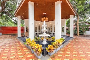 A covered pavilion with a central fountain, surrounded by potted plants and a patterned floor.