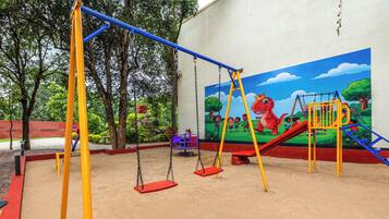 A playground with swings, a slide, and a mural of children playing.