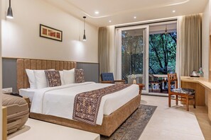 A hotel room with a bed, a desk, a chair, and a view of trees through a glass door.