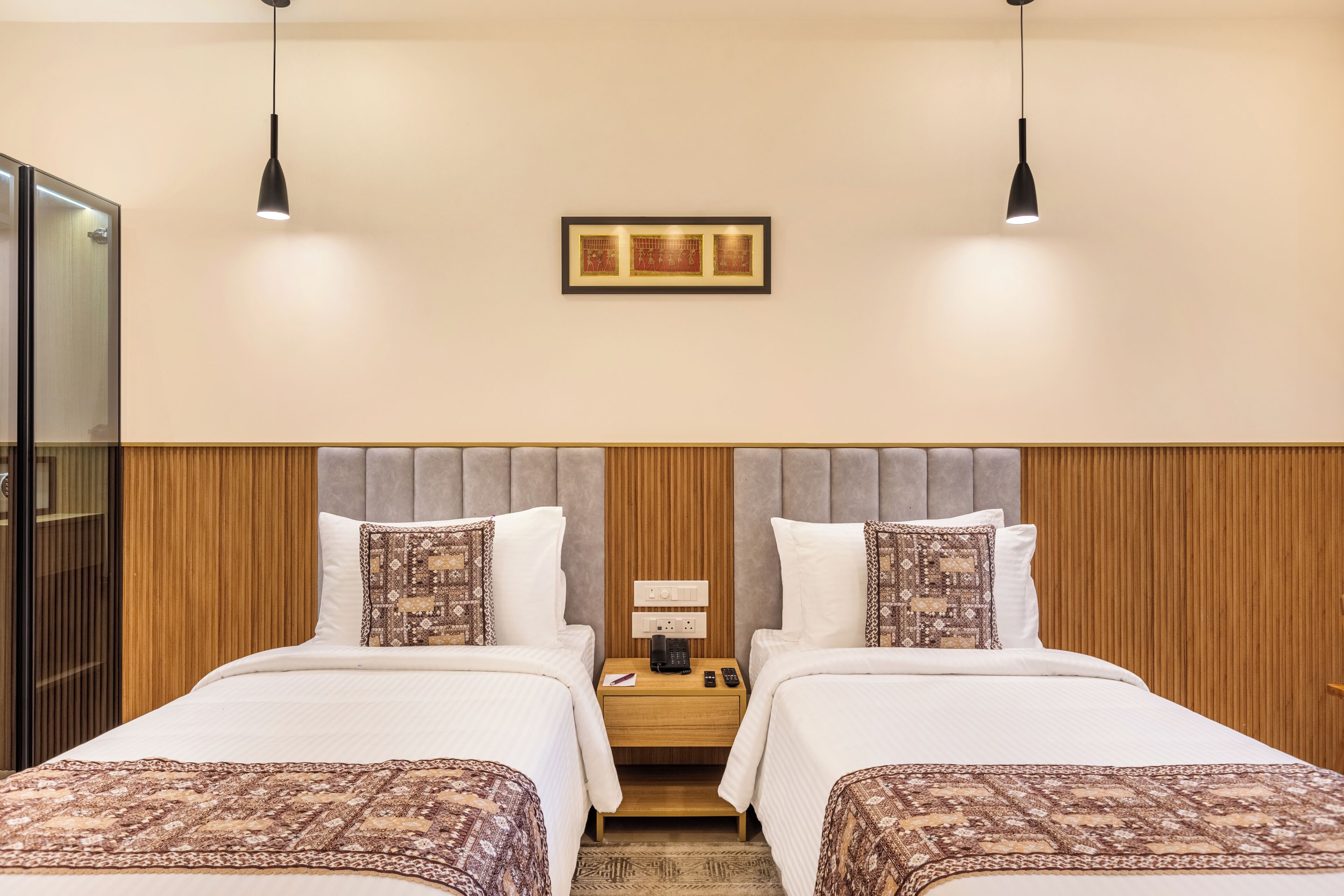 Ein Hotelzimmer mit zwei Betten, einem hölzernen Kopfteil, einem Nachttisch mit Lampe und einem gerahmten Bild an der Wand.