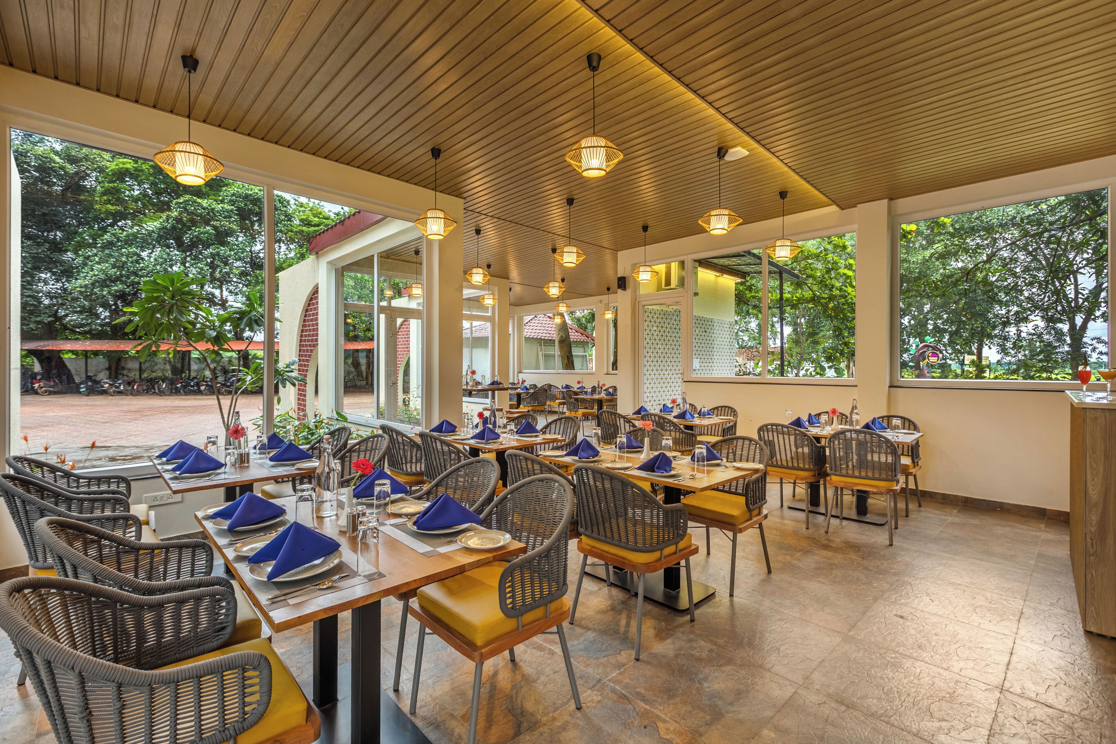 A restaurant with multiple tables and chairs, large windows, and a wooden ceiling.