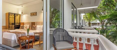 A hotel room with a balcony, a dining table with a sandwich and drinks, and a view of greenery outside.