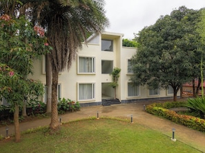 Un edificio de varios pisos con techo plano, rodeado de vegetación y un césped cuidado.