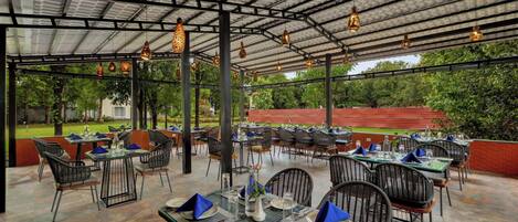 An outdoor dining area with tables and chairs, under a covered roof with hanging lights.