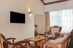 A room with a wooden coffee table, two upholstered chairs, a television mounted on the wall, and a window with curtains. - Sterling Naman Bastar Jagdalpur (Jagdalpur)