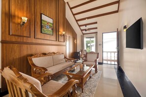 Un salón amplio con paneles de madera, un sofá, sillones, una mesa de centro y un televisor de pantalla plana montado en la pared.