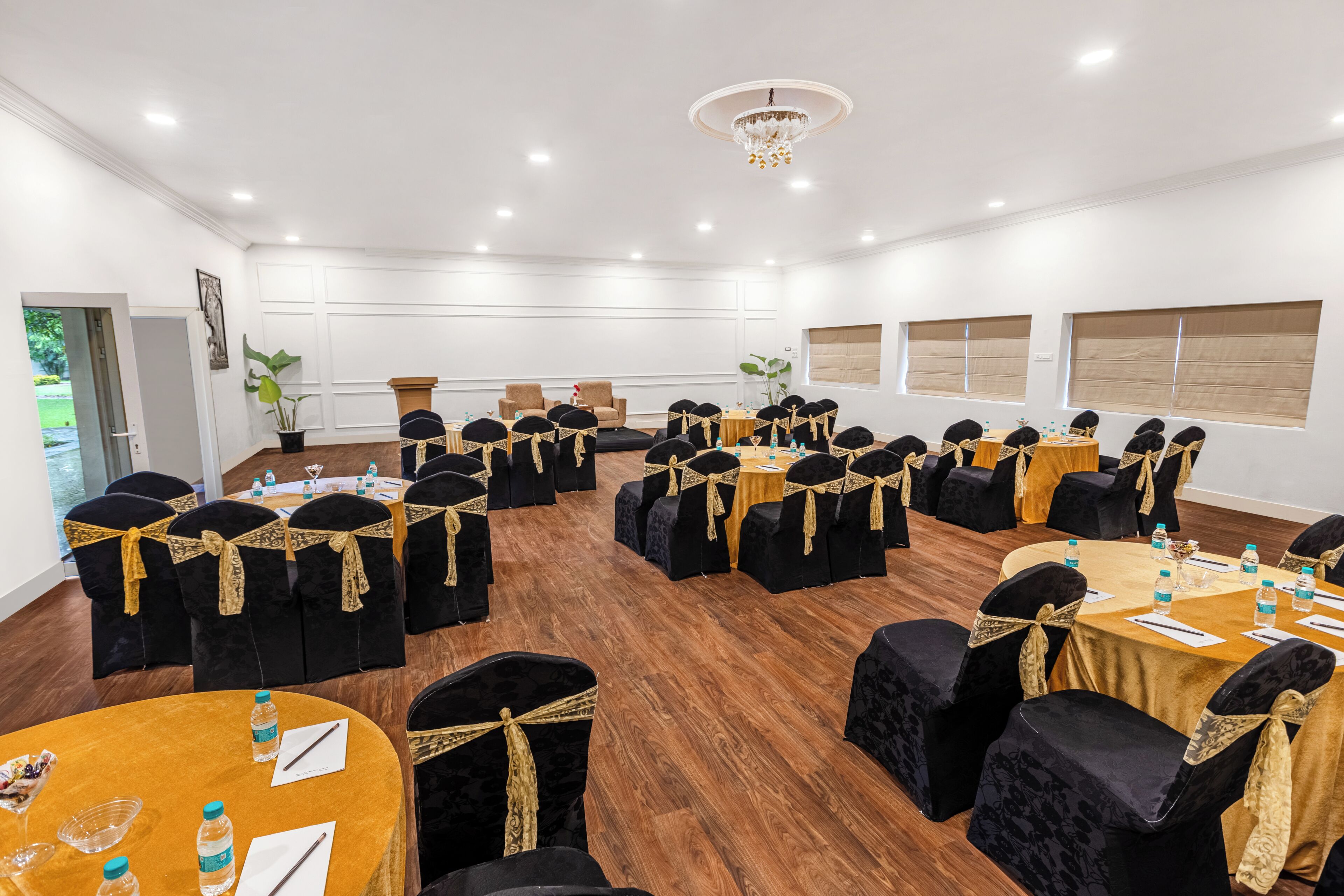 A conference room with round tables, black chairs with gold sashes, and a chandelier.