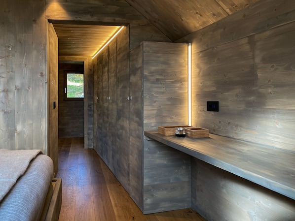 A wooden interior with a bench, a shelf with boxes, and a door leading to a bright outdoor area.