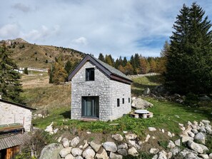 A stone house with a gabled roof, surrounded by a rocky landscape and trees. - AffittiPontediLegno - Chalet Baita Aria (Passo del Tonale)