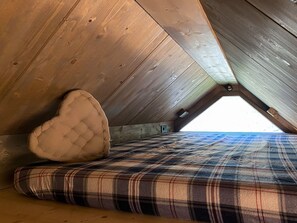 A loft bedroom with a sloped ceiling, a heart-shaped cushion, and a plaid-patterned mattress. - AffittiPontediLegno - Chalet Baita Aria (Passo del Tonale)