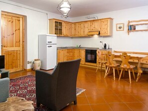 A compact kitchen with wooden cabinets, a built-in oven, and a dining area with a bench and chairs. - AffittiPontediLegno - Qui e Ora House (Ponte di legno)
