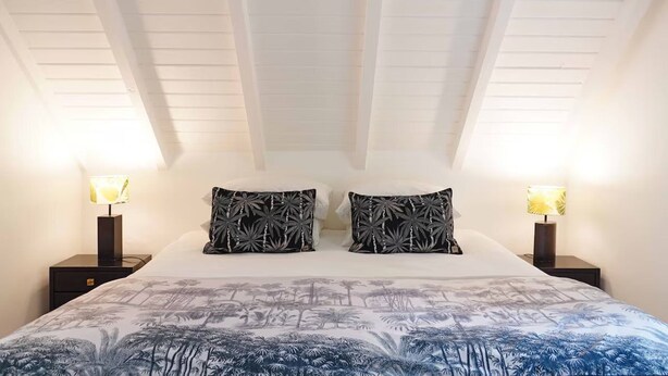 Un dormitorio con techo inclinado, dos lámparas de noche, una cama con colcha estampada y dos almohadas a juego.