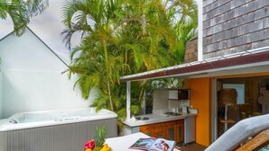 Un espacio exterior privado con jacuzzi, una silla de descanso y una mesa de comedor con fruta.
