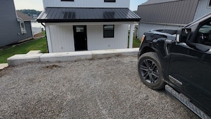 A two-story building with a black roof, a gravel driveway, and a parked black vehicle.