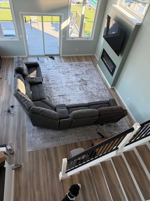 Una sala de estar moderna con un sofá modular, una alfombra grande y una escalera que lleva a una terraza al aire libre.