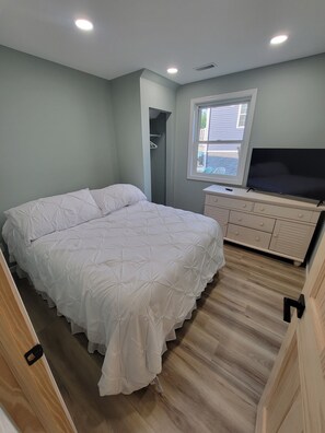 A bedroom with a bed, a dresser, a television, and a window.