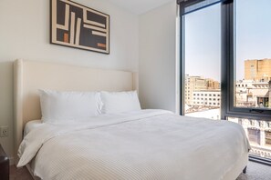 A hotel room with a large bed, a view of the city through a window, and a piece of abstract art on the wall. - Blueground | First Hill, rooftop pool, nr Seattle Art Museum (Seattle)