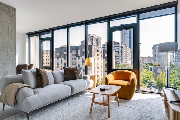 A modern living room with a grey sofa, a small wooden table, and a yellow armchair, featuring large windows with a city view. - Blueground | First Hill, rooftop pool, nr Seattle Art Museum (Seattle)
