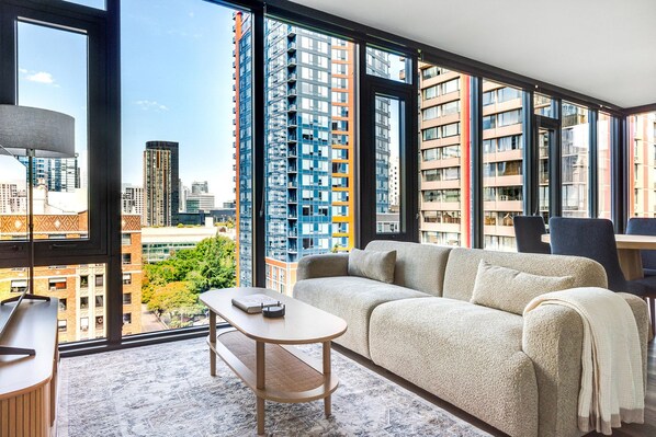 Ein modernes Wohnzimmer mit einer Couch, einem kleinen Tisch und Blick auf hohe Gebäude.
