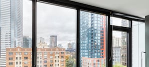 A room with large windows offering a view of a cityscape with high-rise buildings. - Blueground | First Hill, rooftop pool, nr Seattle Art Museum (Seattle)