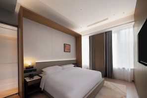 Habitación de hotel con una cama grande, mesitas de noche, un televisor de pantalla plana y una ventana con cortinas.