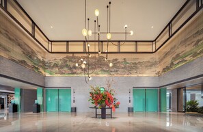 Un hall espacioso con techo alto, luminarias modernas y un arreglo floral central.
