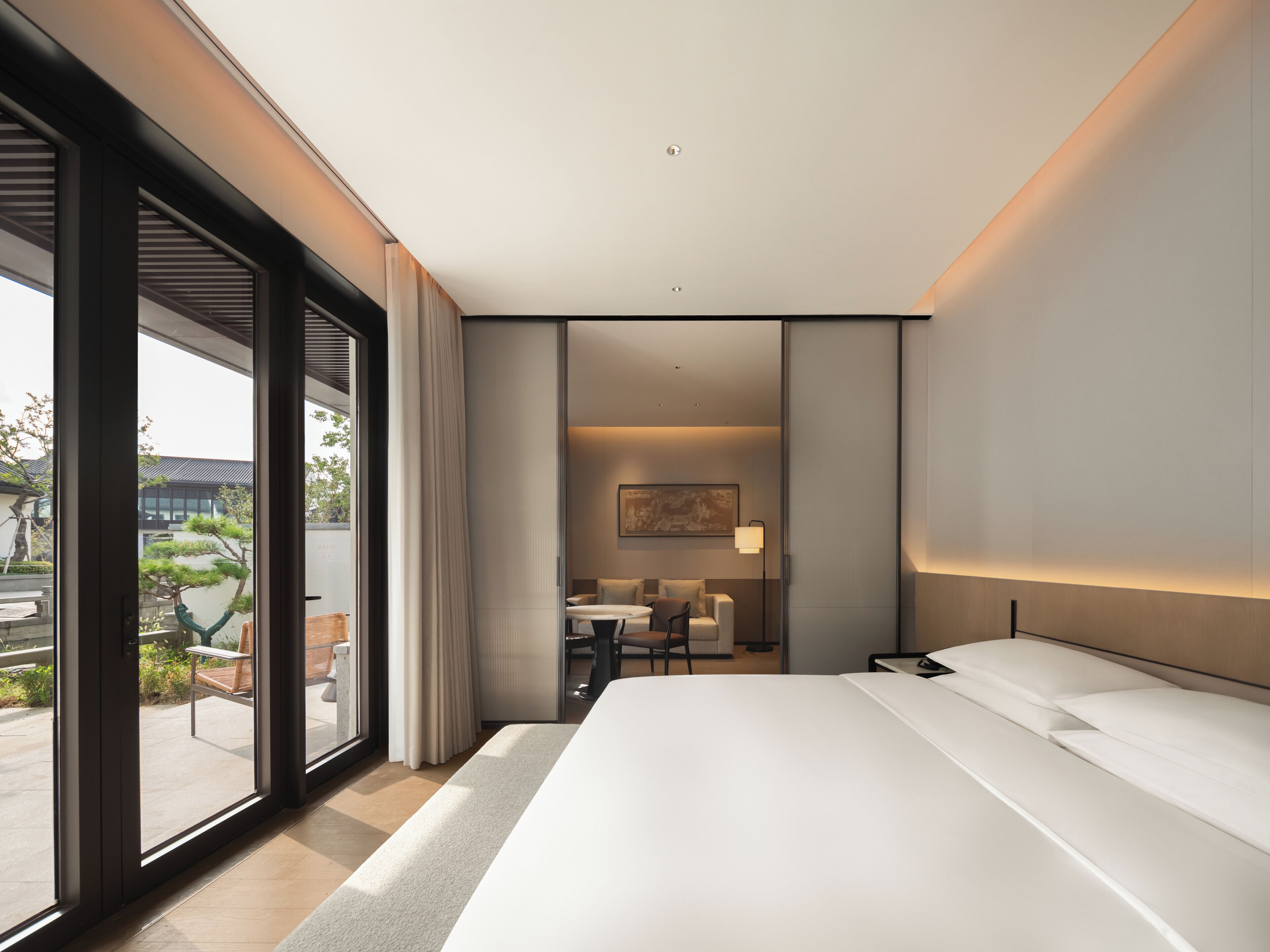 A modern hotel room with a large bed, a desk, and a view of the outdoors.