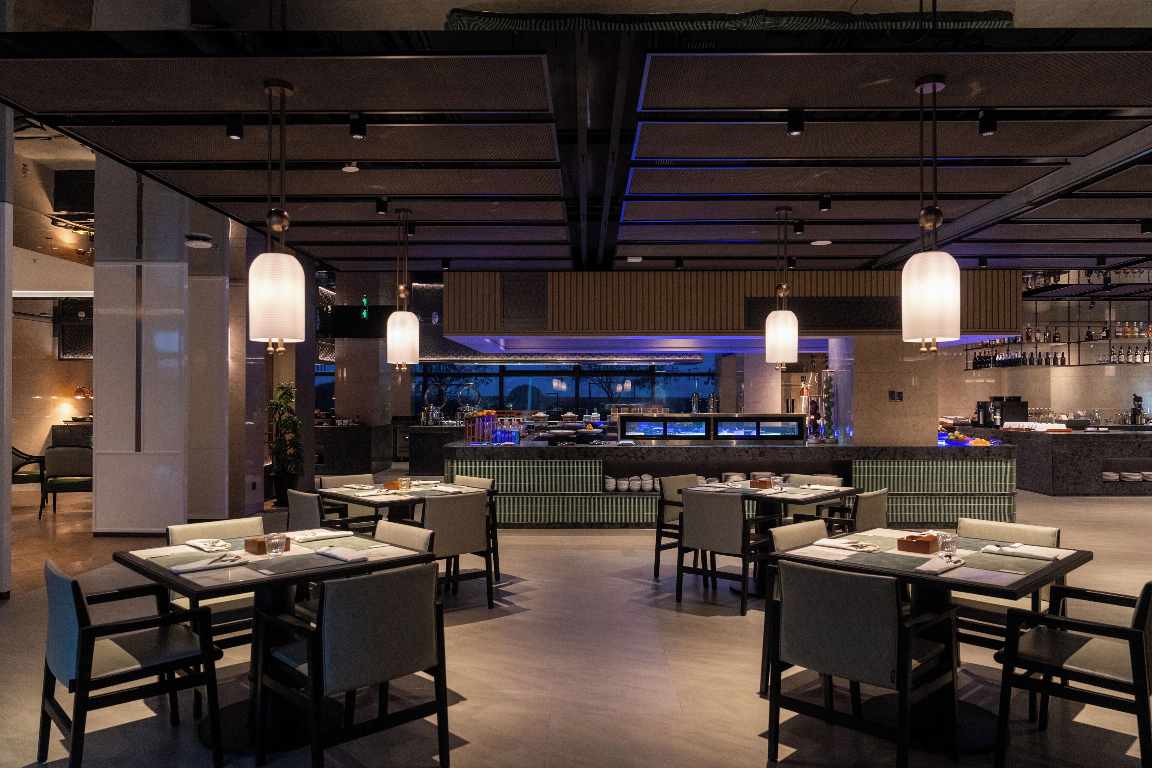 A modern restaurant interior with a bar area, dining tables, and hanging pendant lights.