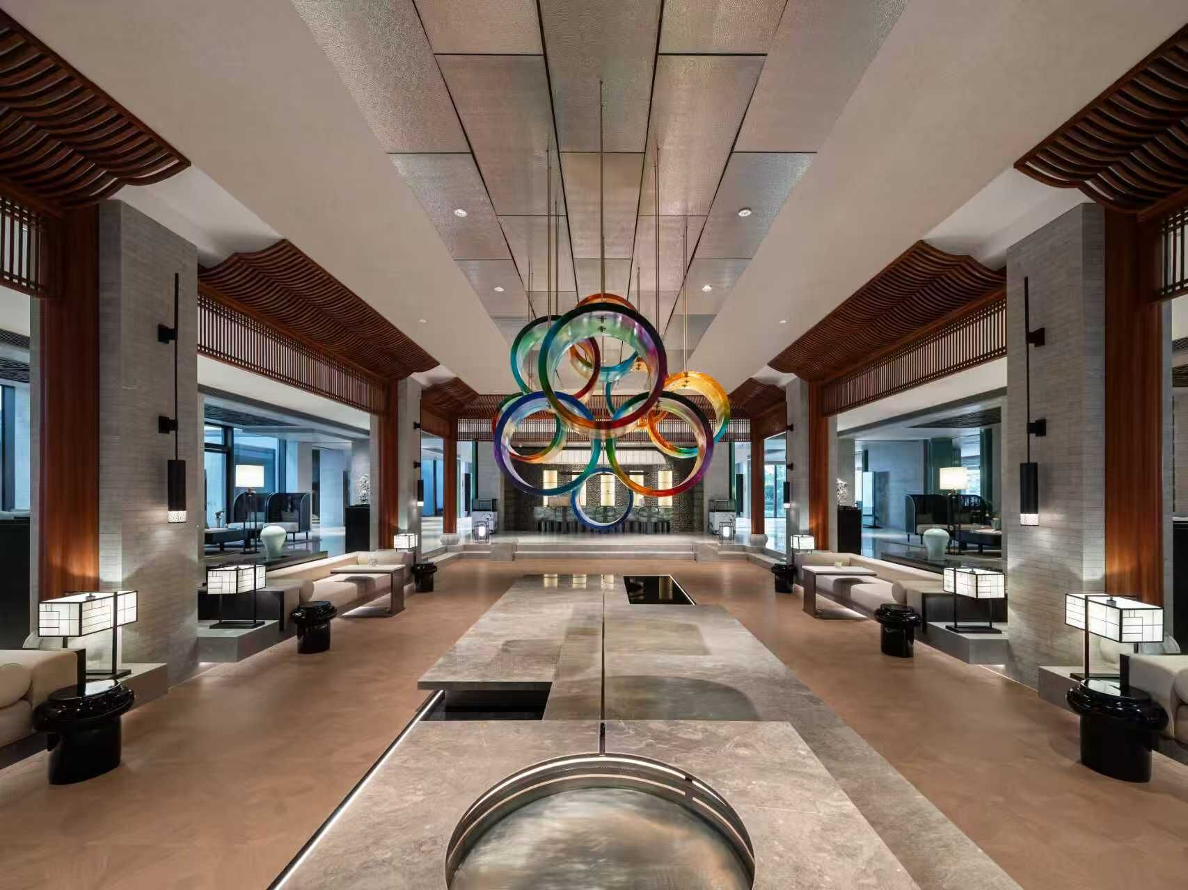 A spacious lobby with a central circular light fixture, seating areas, and a modern architectural design.
