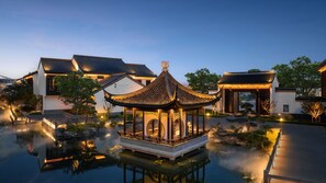 A traditional pavilion over a reflective water body, surrounded by modern buildings with a well-maintained garden.
