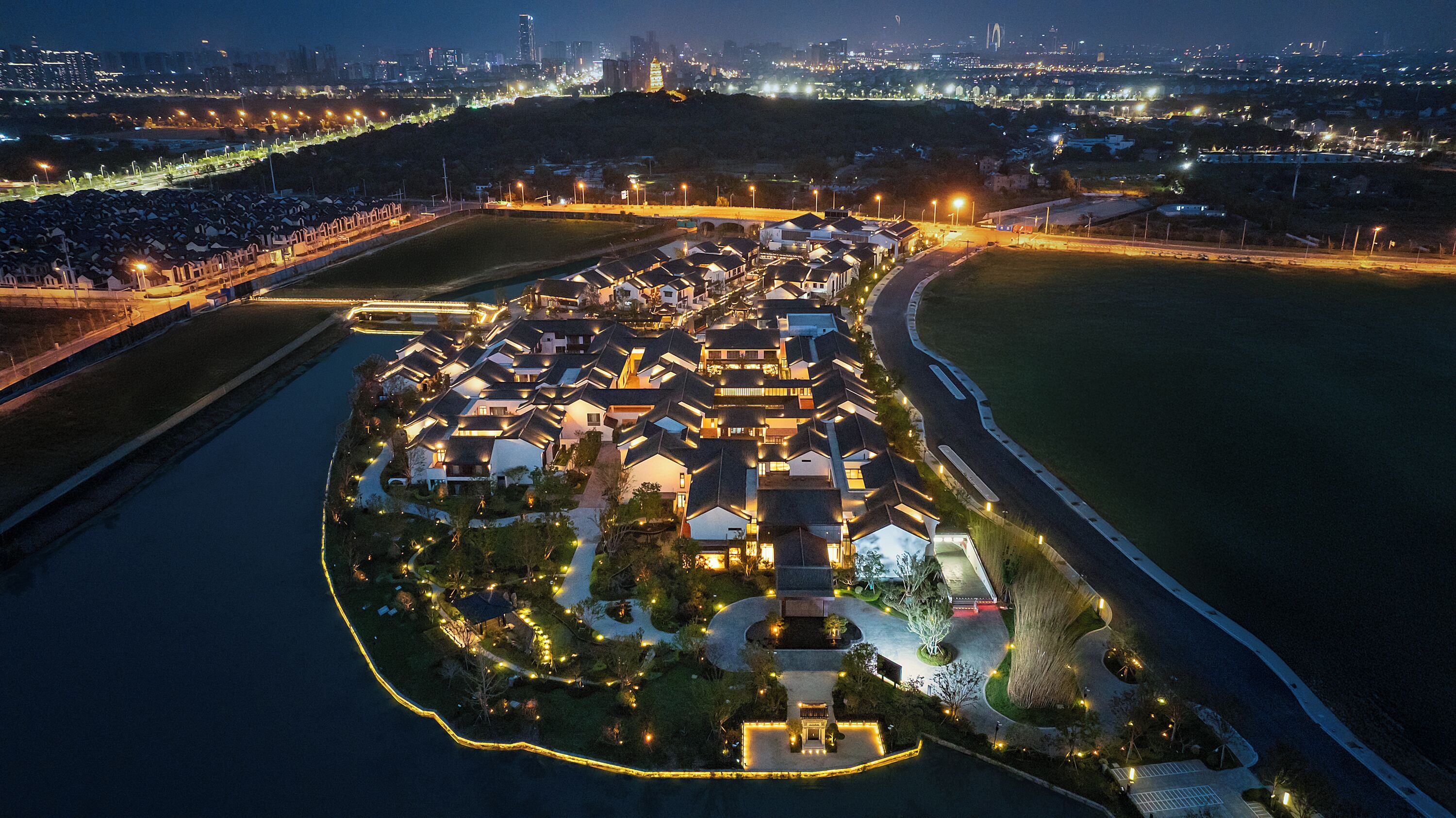 An aerial view of a residential area with houses, a curved road, and a body of water.