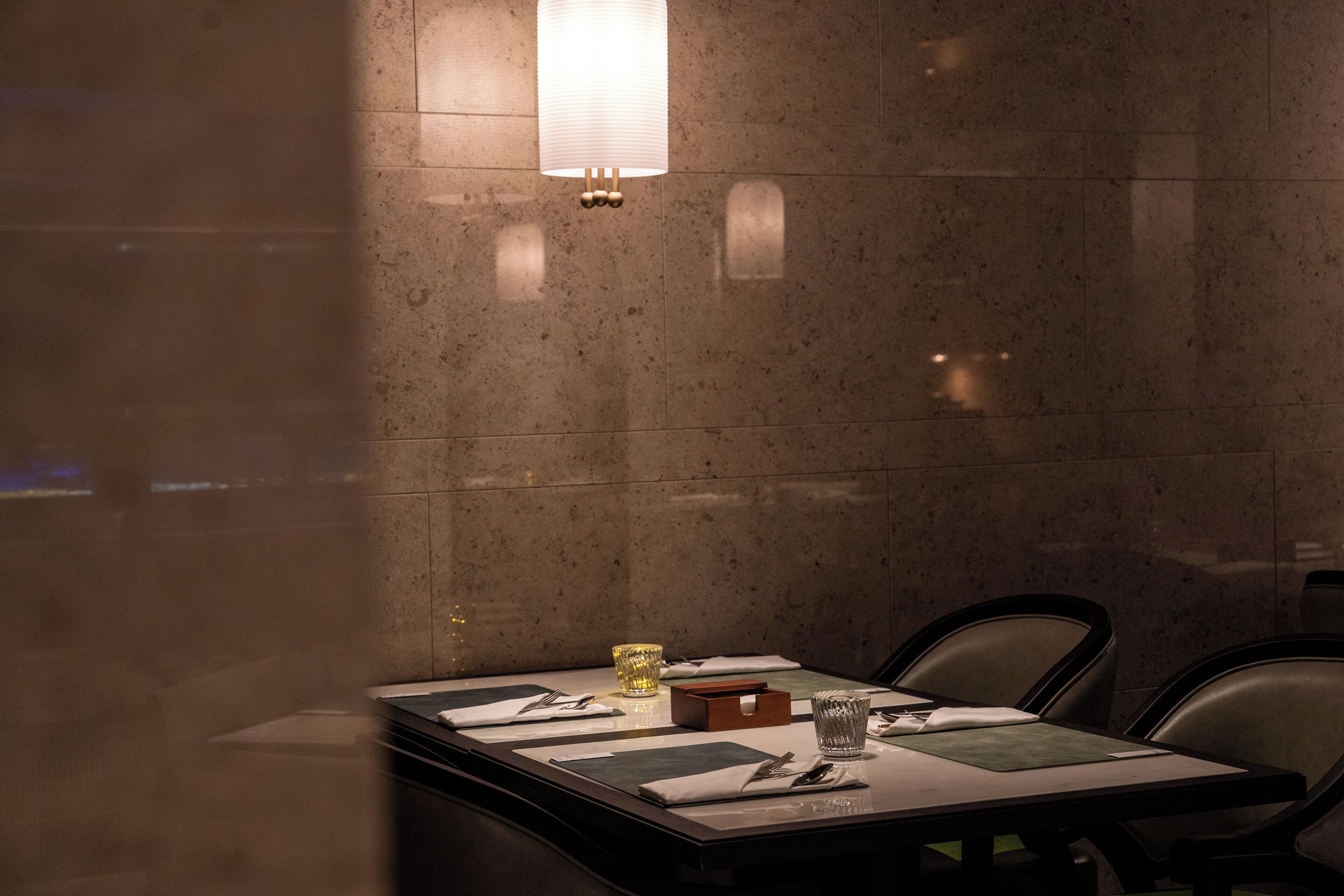 A dimly lit restaurant with a table set for two, featuring a candle, cutlery, and a glass.