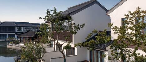 Un bâtiment de style traditionnel agrémenté d’une extension moderne, un plan d’eau à l’avant et un pont en bois.