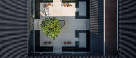 An aerial view of a courtyard with a central tree, surrounded by seating areas and enclosed spaces.