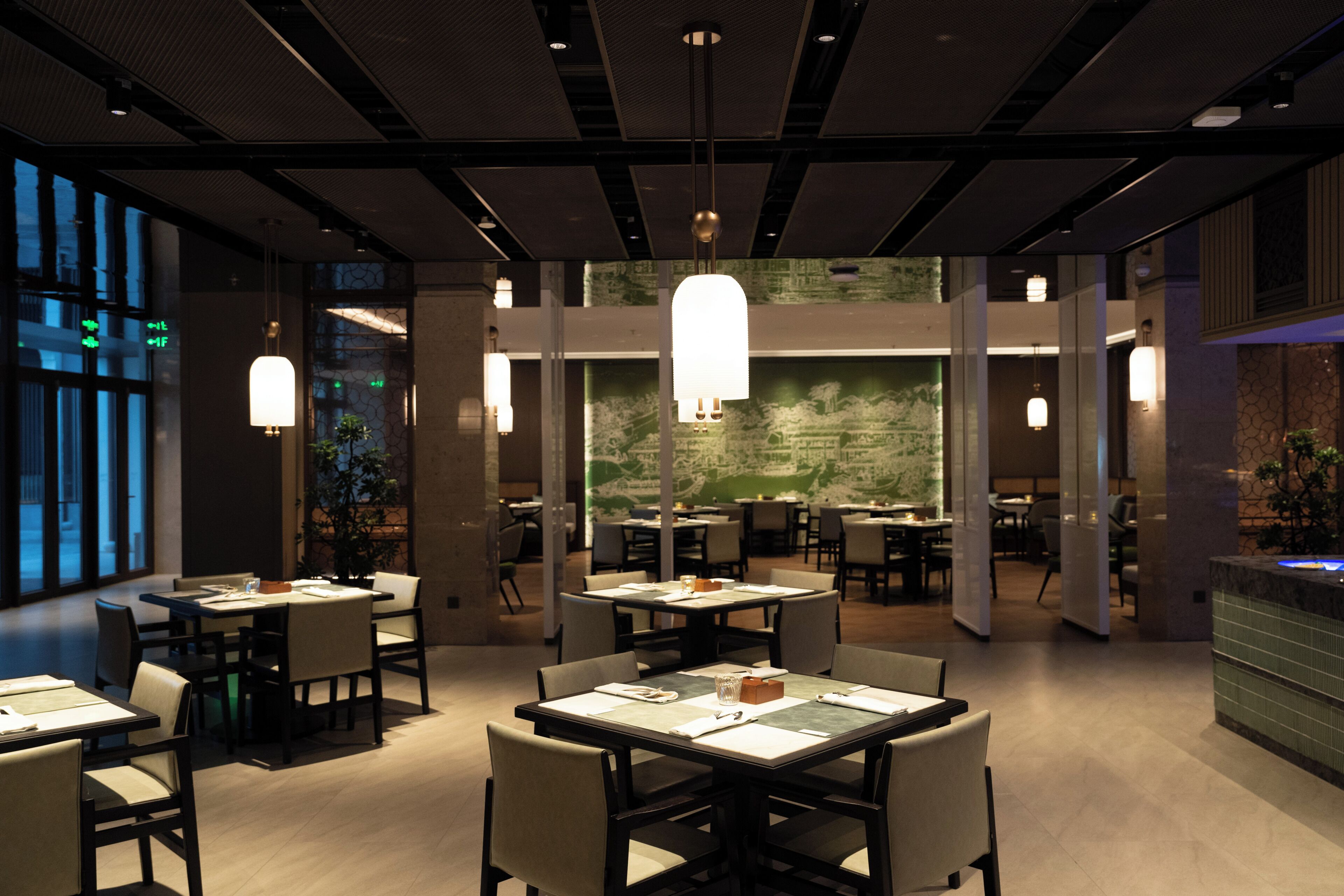 A modern restaurant interior with multiple dining tables and chairs, ambient lighting, and a large mural on the back wall.