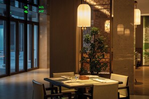 A dining area with a table set for two, a potted plant, and a view of the street outside.