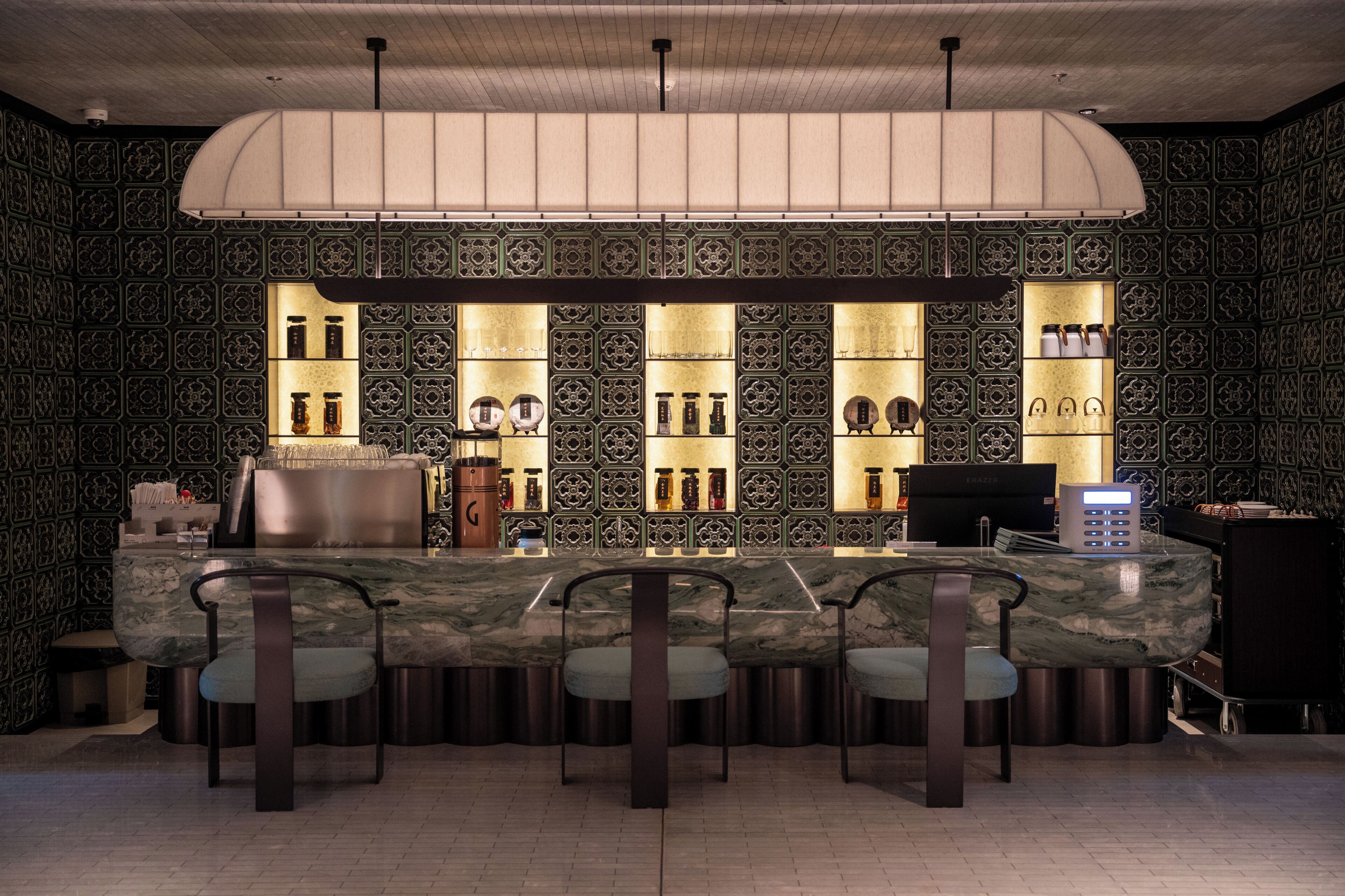 A bar area with a marble counter, three chairs, and shelves with bottles and glasses.