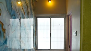 Una habitación con ventana, una pared con diseño de mármol, un cubo de basura verde y un felpudo marrón en el suelo.