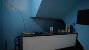 Una habitación pequeña con escritorio, silla y cama. Hay un código QR en la pared y una estantería con varios objetos.