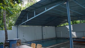 Zona de piscina exterior con área de descanso cubierta y una mesa.